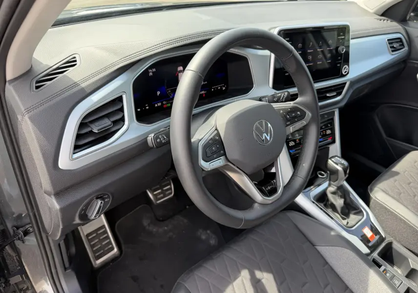 Vue intérieure côté conducteur du Volkswagen T-Roc gris 2025, volant cuir multifonction et tableau de bord digital.