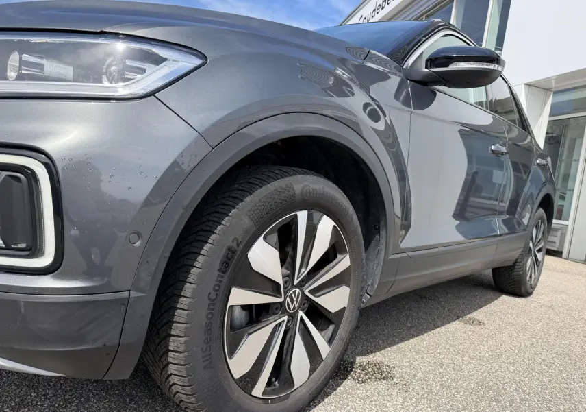 Vue 3/4 avant droit du Volkswagen T-Roc gris mettant en valeur la roue avant et le rétroviseur noir brillant.