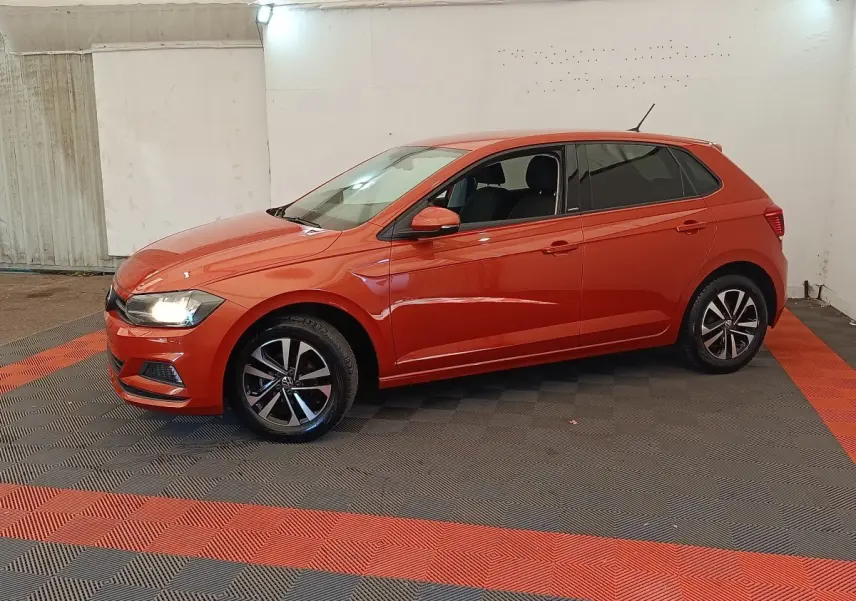 Volkswagen Polo 1.0 TSI orange vue de profil côté gauche, phares allumés, jantes alliage noires et argentées.
