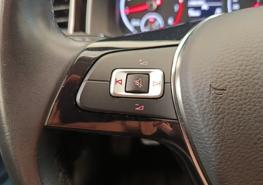 Gros plan sur les commandes du volant cuir et alu de la Volkswagen Polo 1.0 TSI 95 United, avec indicateurs rouges.