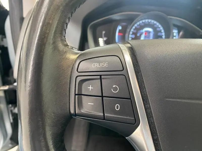 Gros plan sur les commandes de régulateur de vitesse au volant cuir noir d'un Volvo XC60 argenté de 2015.