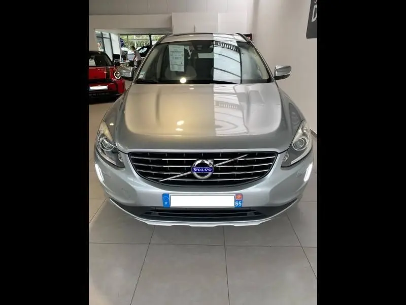 Vue de face d'un Volvo XC60 argenté en showroom, avec calandre distinctive et phares allumés.