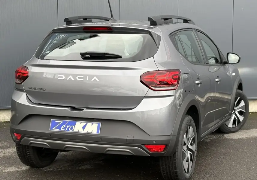 Vue 3/4 arrière droite d'une Dacia Sandero Stepway 2025 gris schiste avec barres de toit et feux arrière LED en Y.