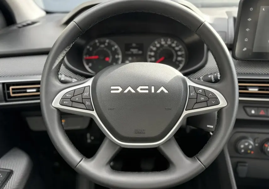 Volant noir de la Dacia Sandero Stepway 2025 vu de face, avec commandes intégrées et tableau de bord en arrière-plan.