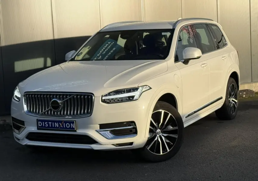 Volvo XC90 blanc Crystal en 3/4 avant droit, avec jantes alliage noires et contours chromés visibles.