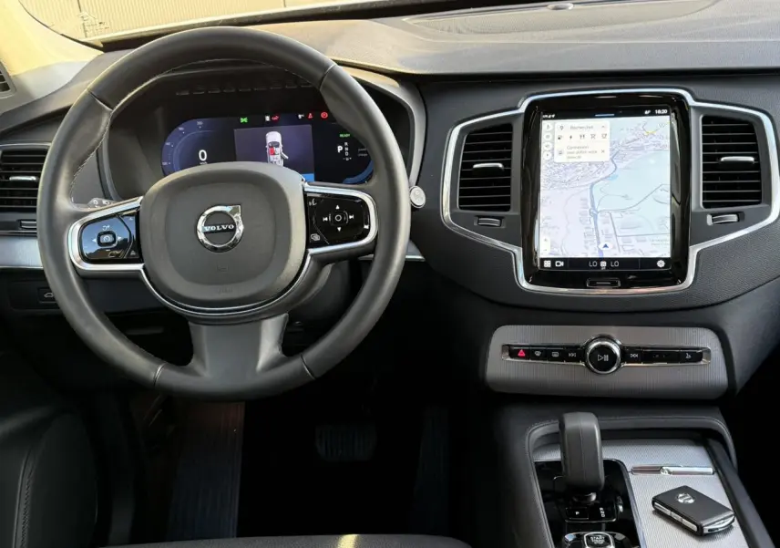 Vue de face de l'intérieur du Volvo XC90 blanc Crystal 2024, volant cuir et écran tactile central avec navigation.