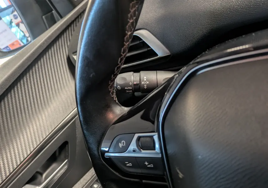 Gros plan sur le volant et la commande de régulation du volume du Peugeot 3008 gris Arthense, intérieur côté conducteur.