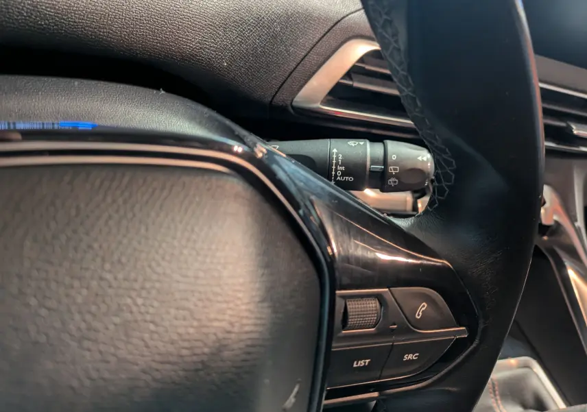 Gros plan sur les commandes au volant en cuir noir du Peugeot 3008 gris Arthense, avec réglages audio et téléphone visibles.