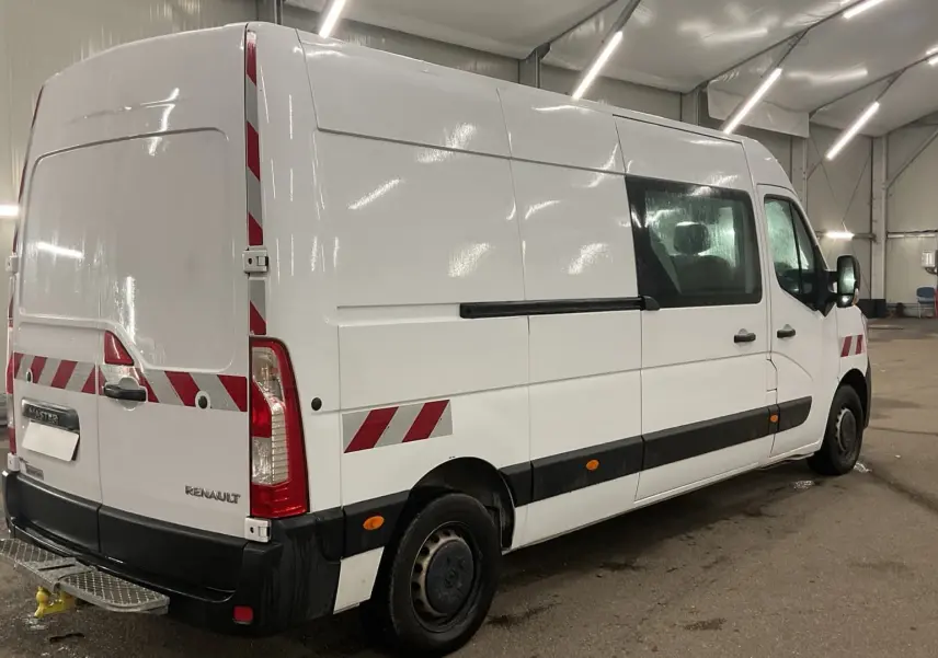 Vue 3/4 arrière droite d’un Renault Master blanc avec marquages réfléchissants rouges et blancs dans un garage.