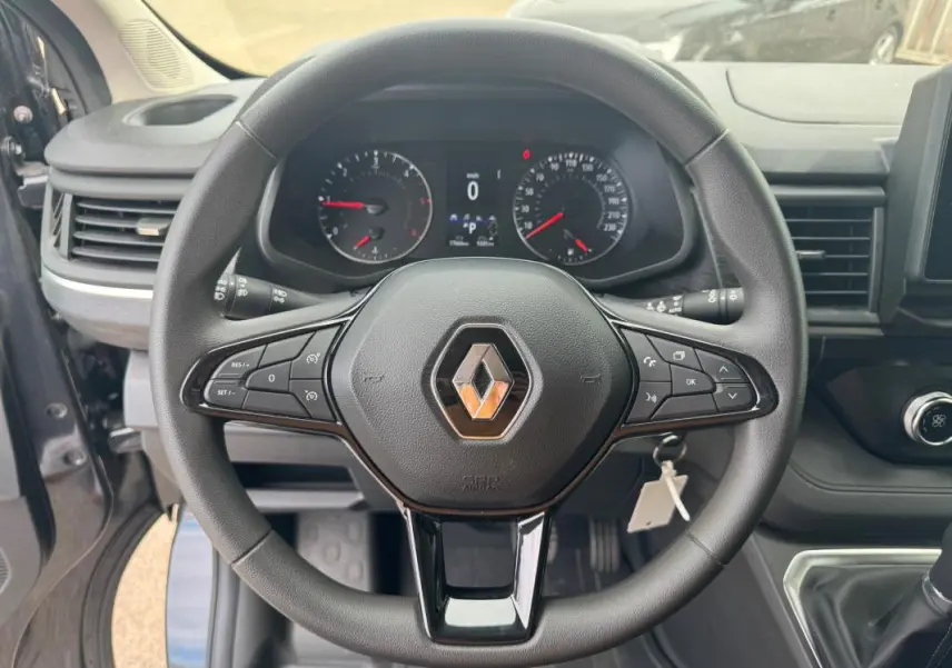 Vue rapprochée du volant noir avec logo Renault du Trafic Fourgon gris foncé, tableau de bord et commandes visibles.