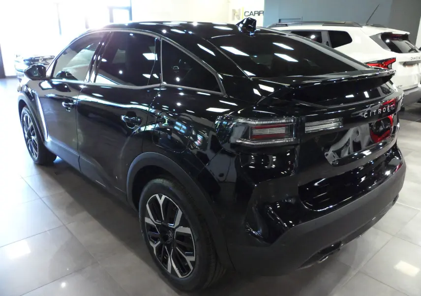 Vue 3/4 arrière côté gauche d'une Citroën C4 Hybride 2025 noire Perla avec jantes alliage et vitres teintées.