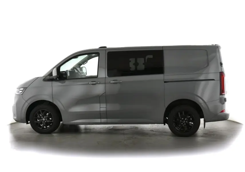 Vue de profil côté gauche d’un Volkswagen Transporter T7 gris Stone avec jantes alliage noir brillant et vitres arrière surteintées.