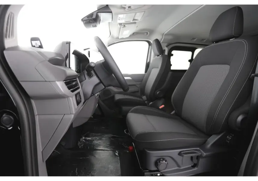 Vue intérieure côté conducteur du Volkswagen Transporter T7 2025, sièges tissu noir à rayures avec volant multifonction.