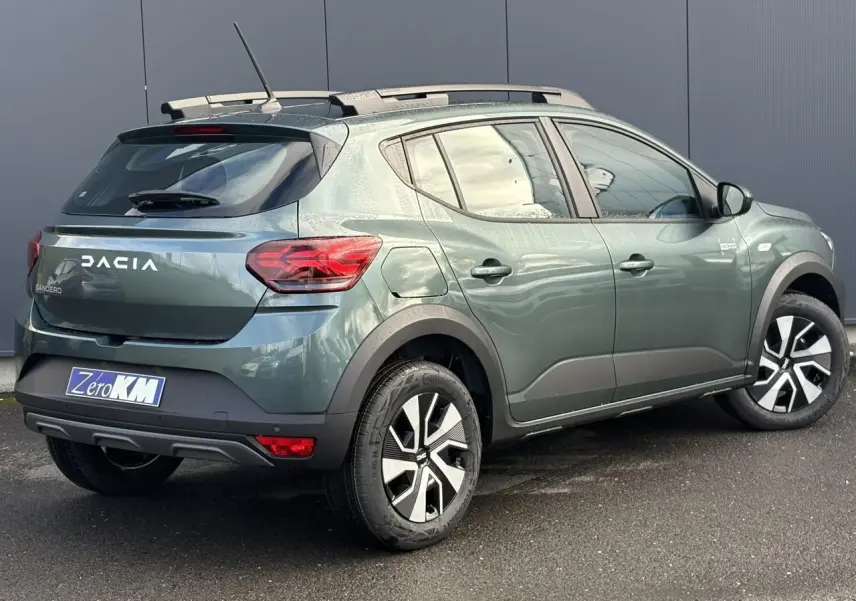 Vue 3/4 arrière droite d'une Dacia Sandero Stepway 2025 vert cèdre avec barres de toit et jantes spécifiques.