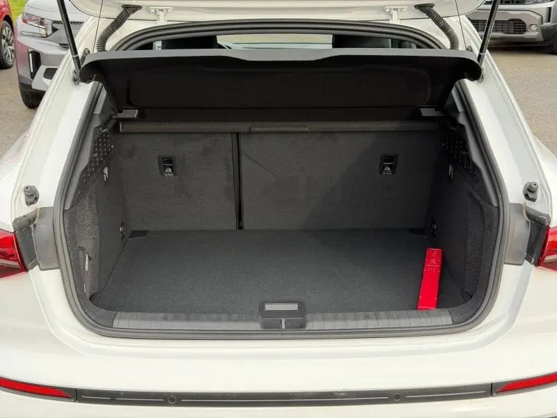 Coffre ouvert vu de l'arrière d'une Audi A3 Sportback blanc Arkona 2024, avec intérieur noir et triangle de sécurité rouge.