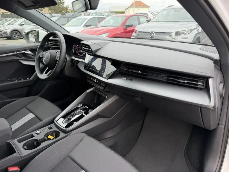 Vue intérieure côté passager de l'Audi A3 Sportback 2024, tableau de bord moderne avec écran tactile et sellerie tissu noir.