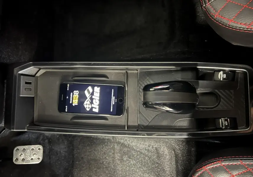 Vue plongeante sur la console centrale noire de la Ligier JS50 bleu, avec levier de vitesse et smartphone posé.