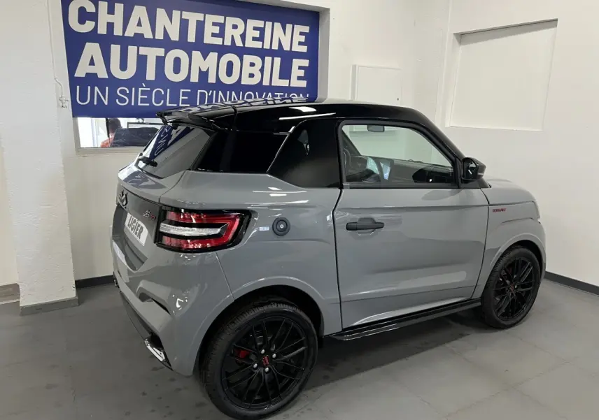 Vue 3/4 arrière droite d'une LIGIER JS50 gris clair avec toit noir brillant et jantes noires en intérieur showroom.