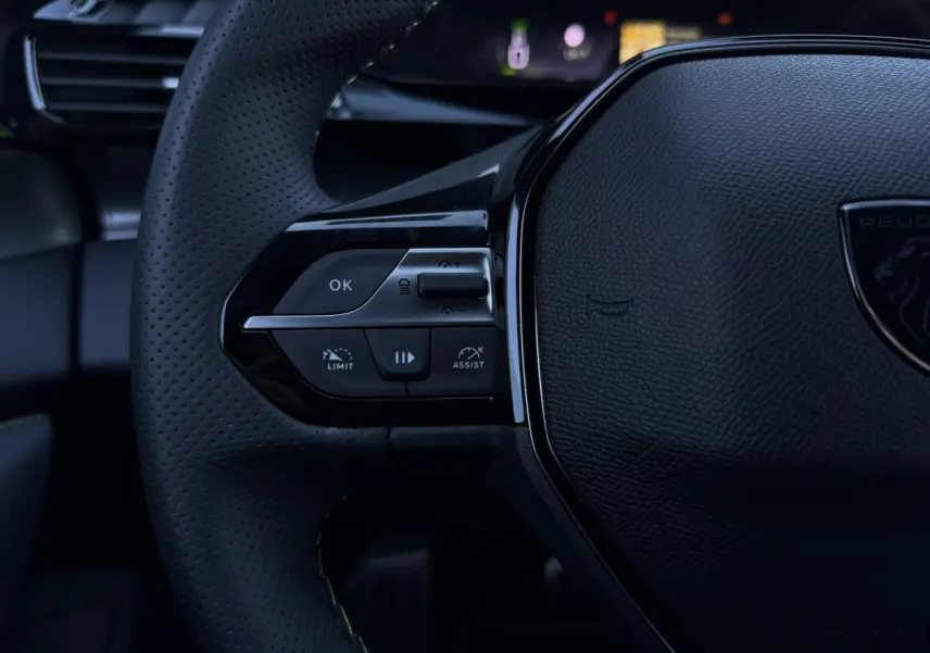 Gros plan sur le volant perforé noir de la Peugeot 408 Hybrid 145 e-DSC6 GT avec commandes intégrées côté gauche.