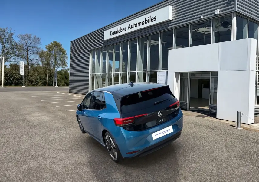 Vue 3/4 arrière droite d'une Volkswagen ID.3 204 ch Pro S 77 kWh bleu métallisé avec toit noir devant un concessionnaire.