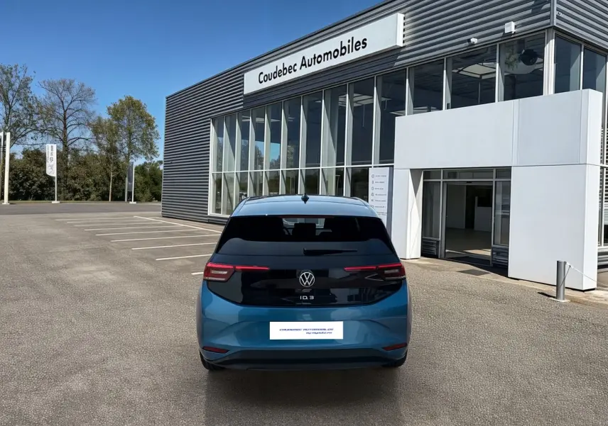 Vue arrière d'une Volkswagen ID.3 bleue métallisée avec toit noir, stationnée devant un bâtiment Coudebec Automobiles.