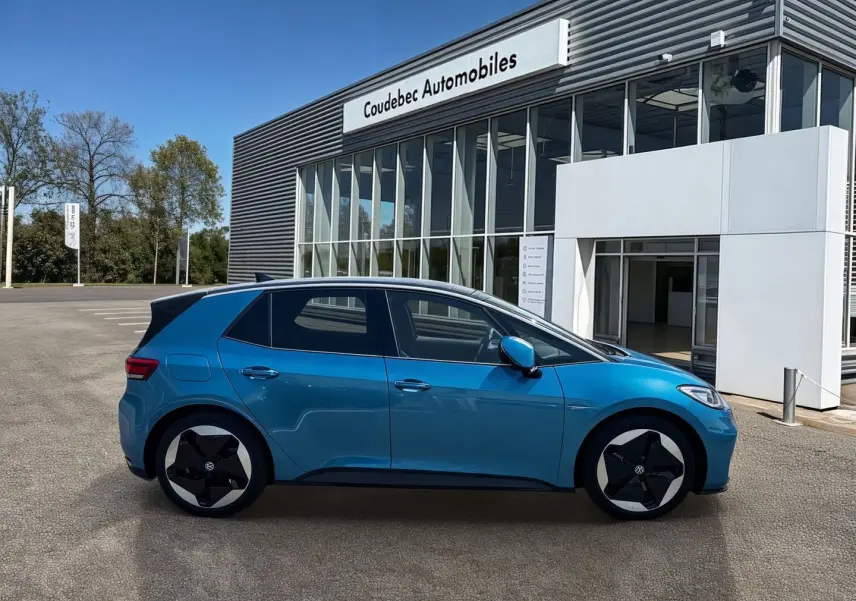 Profil côté gauche d'un Volkswagen ID.3 204 ch Pro S 77 kWh bleu métallisé avec toit noir, stationné devant un bâtiment.