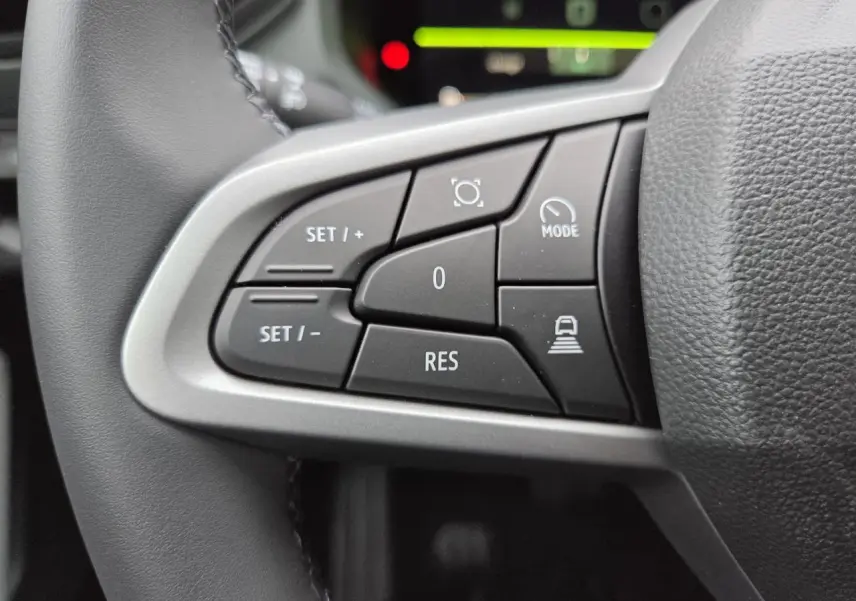 Gros plan sur les commandes au volant à gauche du Dacia Bigster 2025 blanc glacier, avec boutons de régulateur de vitesse et mode conduite.