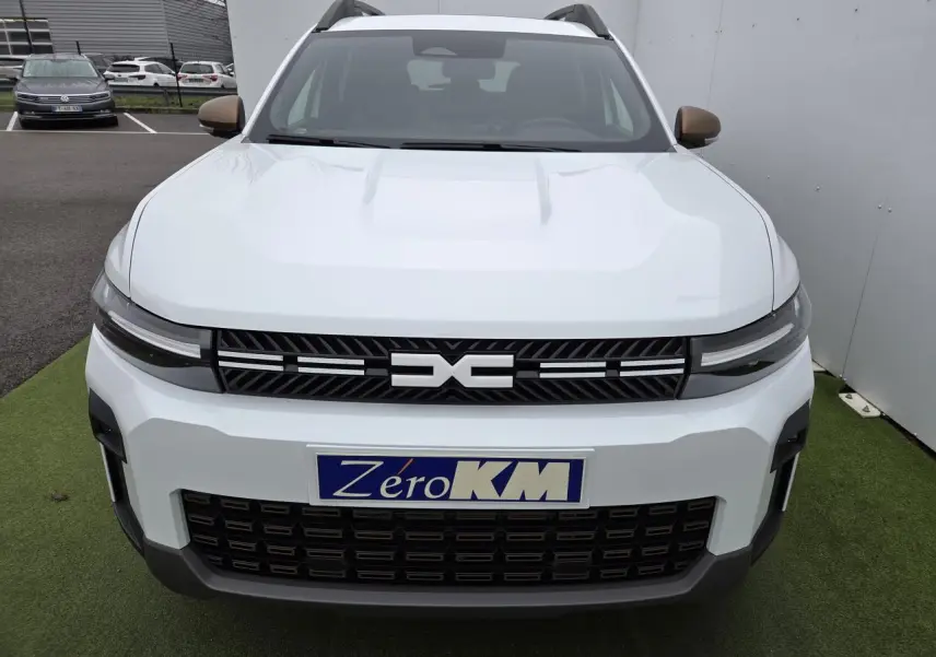 Vue frontale d'un Dacia Bigster blanc glacier avec calandre noire et rétroviseurs brun cuivré visibles.