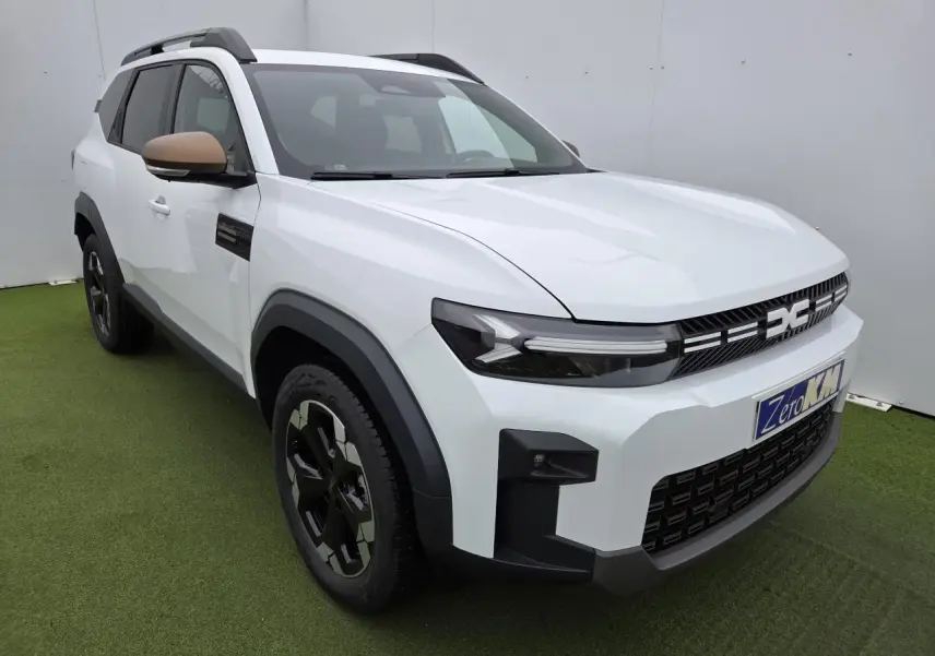 Vue 3/4 avant droit du Dacia Bigster blanc glacier avec calandre et rétroviseurs brun cuivré et jantes noires.