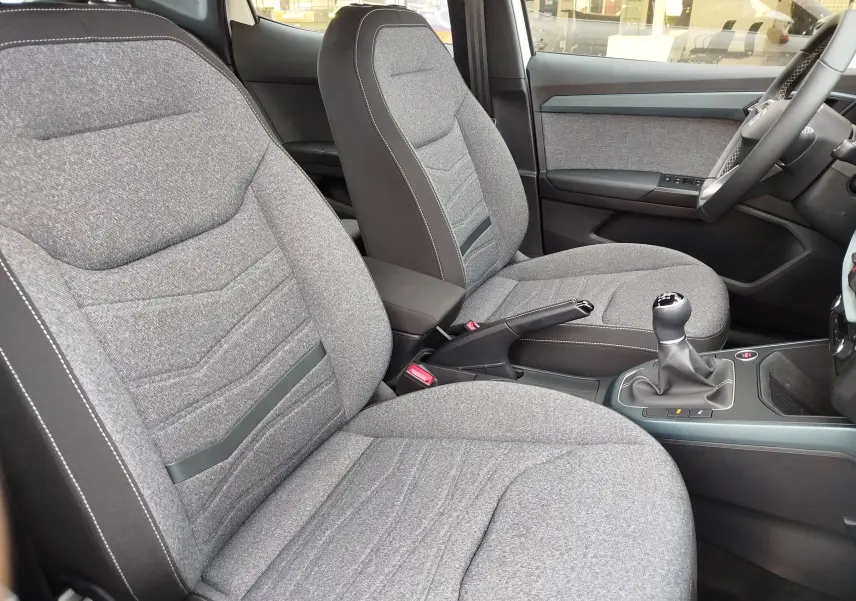 Vue intérieure côté conducteur de la SEAT Arona 2023, sièges tissu gris clair et levier de vitesses manuel.