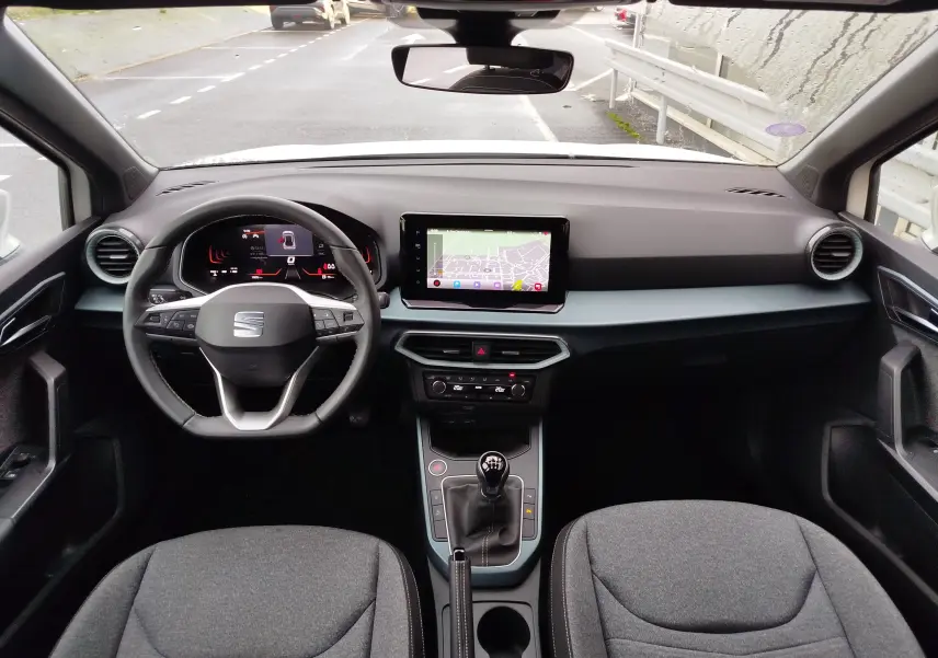 Vue intérieure frontale du tableau de bord et volant du SEAT Arona 2023, avec écran tactile et levier de vitesse manuel.