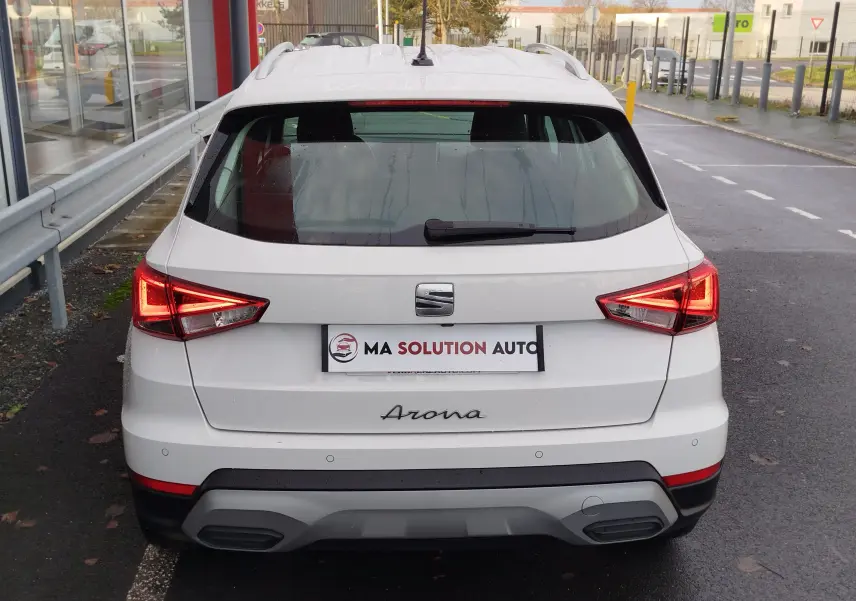 Vue arrière d'un SEAT Arona blanc Candy 2023 avec feux allumés et détails noirs sur le pare-chocs.