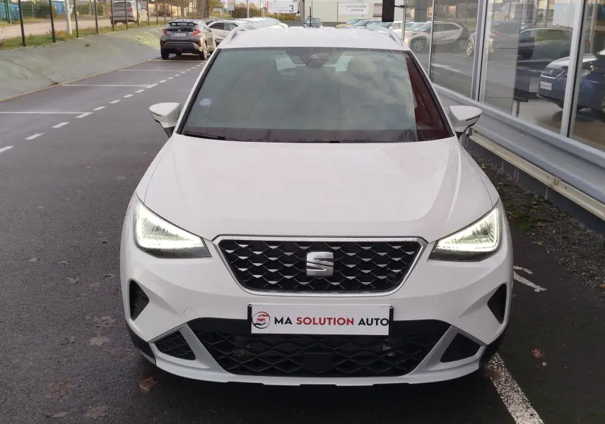 Vue frontale d'un SEAT Arona blanc Candy 2023 avec phares LED allumés, calandre noire et plaque "Ma Solution Auto".