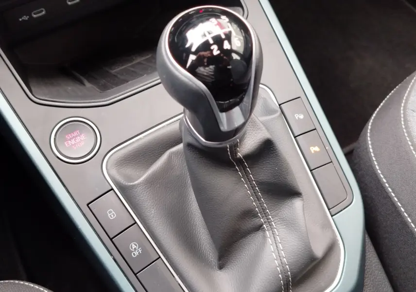 Le levier de vitesses manuel noir avec coutures blanches dans l'habitacle d'une SEAT Arona blanc Candy 2023.