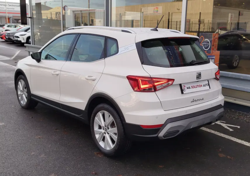Vue 3/4 arrière droite d'un SEAT Arona blanc Candy 2023 avec feux arrière LED et jantes alliage.
