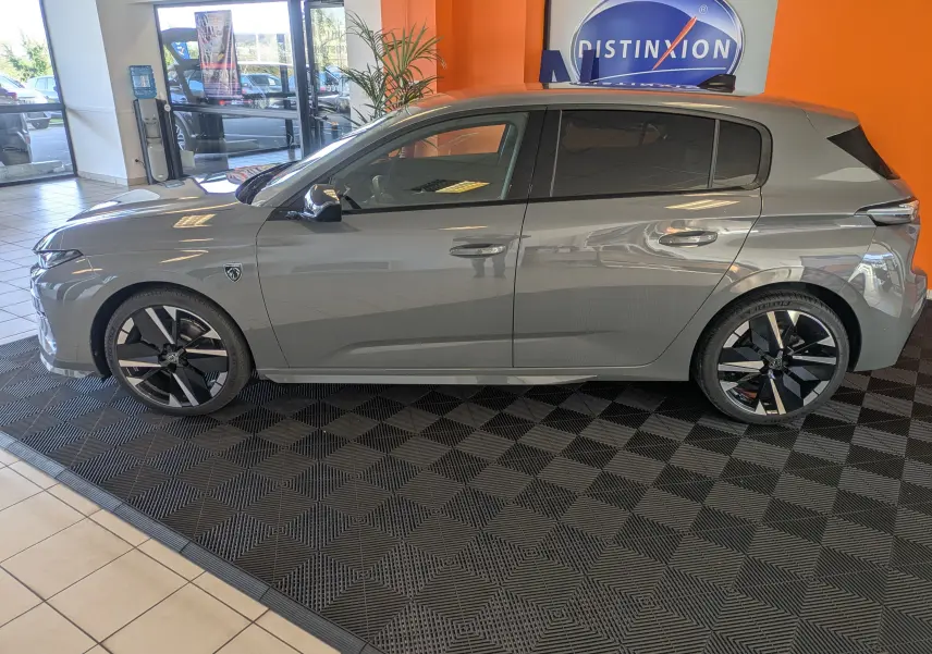 Profil côté gauche du Peugeot 308 gris selenium hybride 2026 en intérieur, soulignant ses jantes noires et détails modernes.