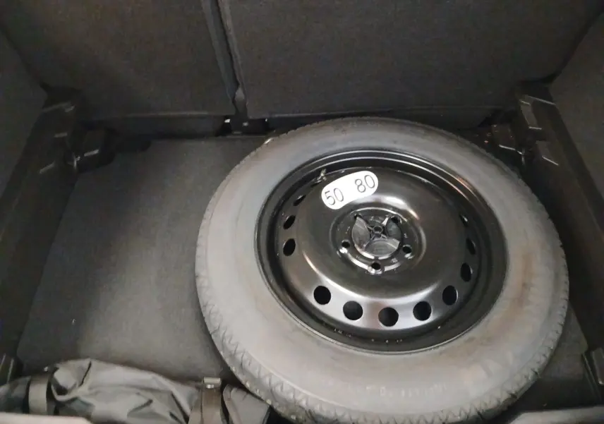 Vue du coffre du Renault Captur E-Tech Full Hybrid 2023 montrant la roue de secours noire sur fond gris cassiopée.