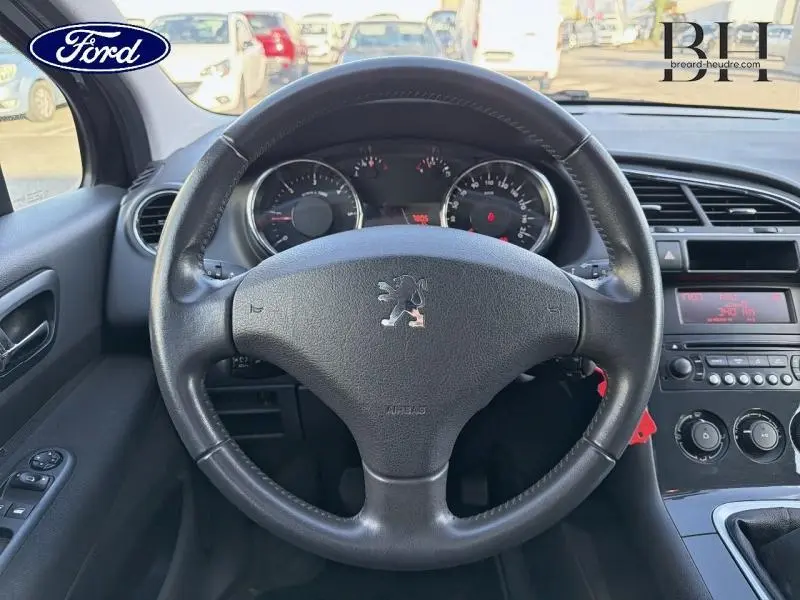 Vue intérieure centrée sur le volant noir avec logo Peugeot, tableau de bord et console centrale d'une 3008 2012.