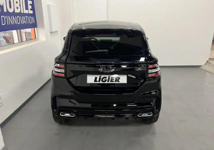 Vue arrière d'une Ligier JS50 noire 2026 avec feux LED et jantes alu noires mates dans un intérieur blanc.