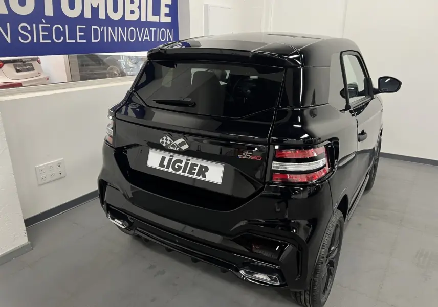 Vue 3/4 arrière droite de la LIGIER JS50 noire avec feux LED et jantes alu noires mates dans un showroom.