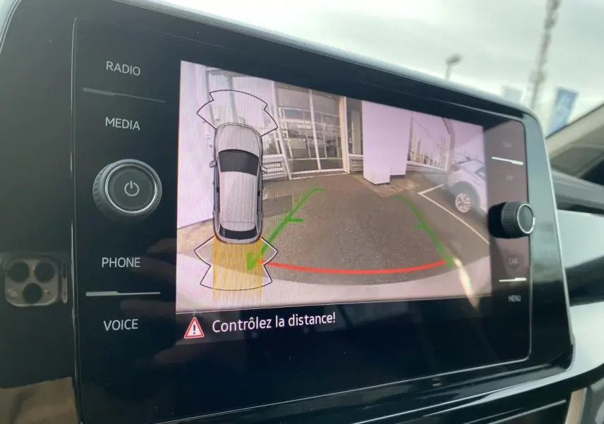 Écran tactile intérieur montrant la caméra de recul avec vue arrière et aide au stationnement du Volkswagen T-Roc gris.