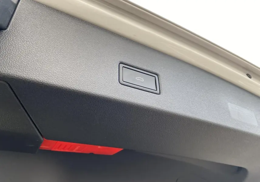 Bouton d'ouverture électrique du coffre sur la partie intérieure de la malle arrière d'une Volkswagen T-Roc grise.