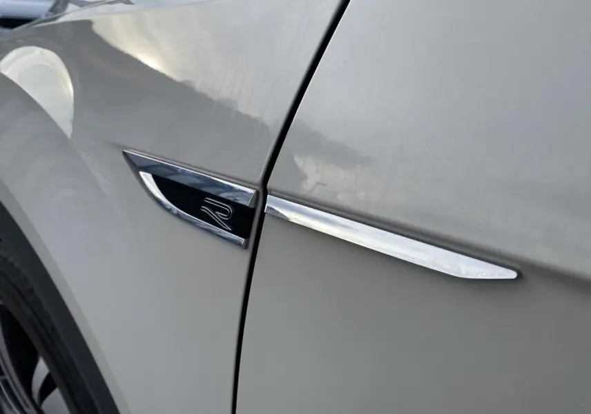 Gros plan sur l'emblème R et la baguette chromée sur l'aile avant gauche du Volkswagen T-Roc gris.