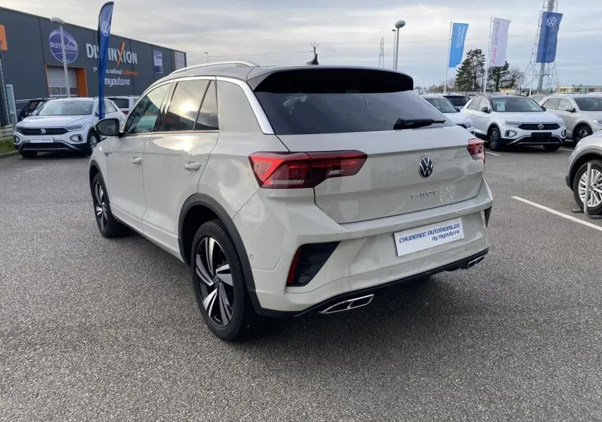 Vue 3/4 arrière droite d'un Volkswagen T-Roc gris clair avec jantes alliage bicolores et vitres arrière teintées.