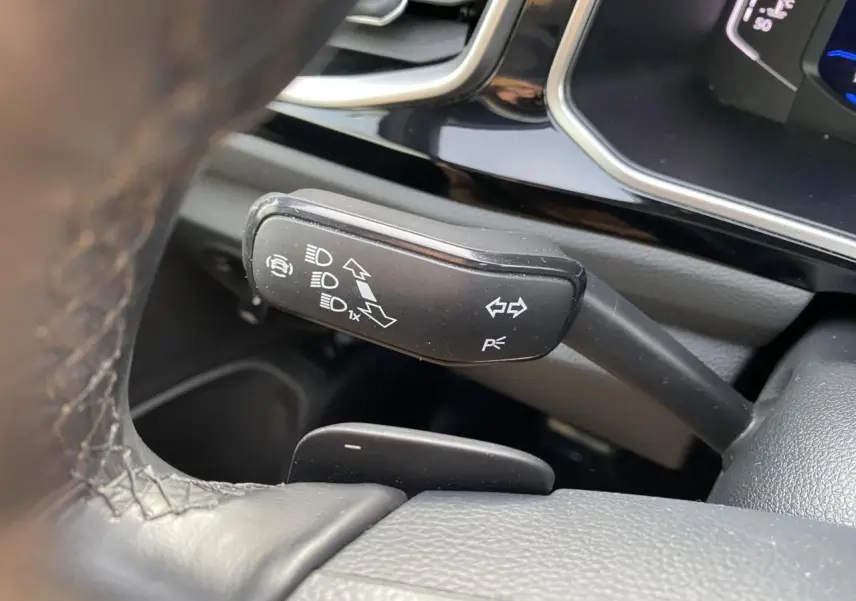 Gros plan sur la manette de clignotant noire à gauche du volant en cuir dans l'habitacle du Volkswagen T-Roc gris.