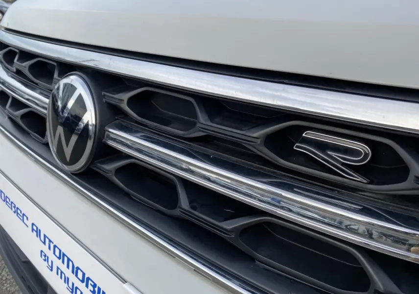 Gros plan sur la calandre avant grise du Volkswagen T-Roc avec logo VW et emblème R visible.
