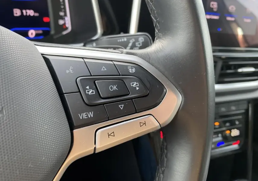 Gros plan sur les commandes gauche du volant cuir noir du Volkswagen T-Roc 2024 avec boutons multifonctions.