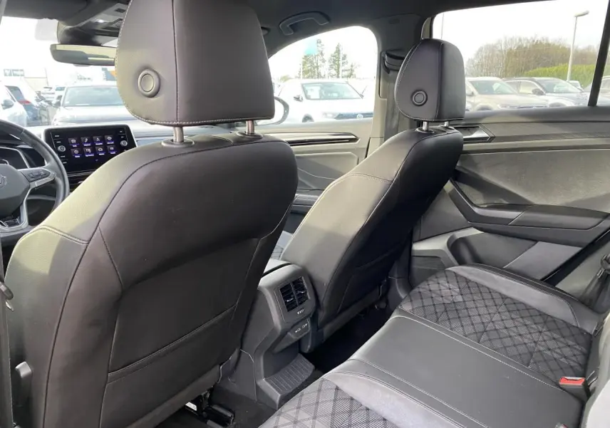 Vue intérieure arrière du Volkswagen T-Roc 2024 gris, montrant les sièges avant en similicuir noir et la banquette arrière avec surpiqûres.