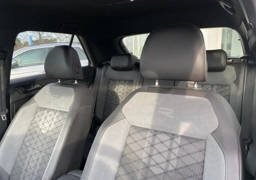 Vue intérieure des sièges avant et arrière du Volkswagen T-Roc 2024 avec sellerie mixte cuir et tissu gris à motif géométrique.