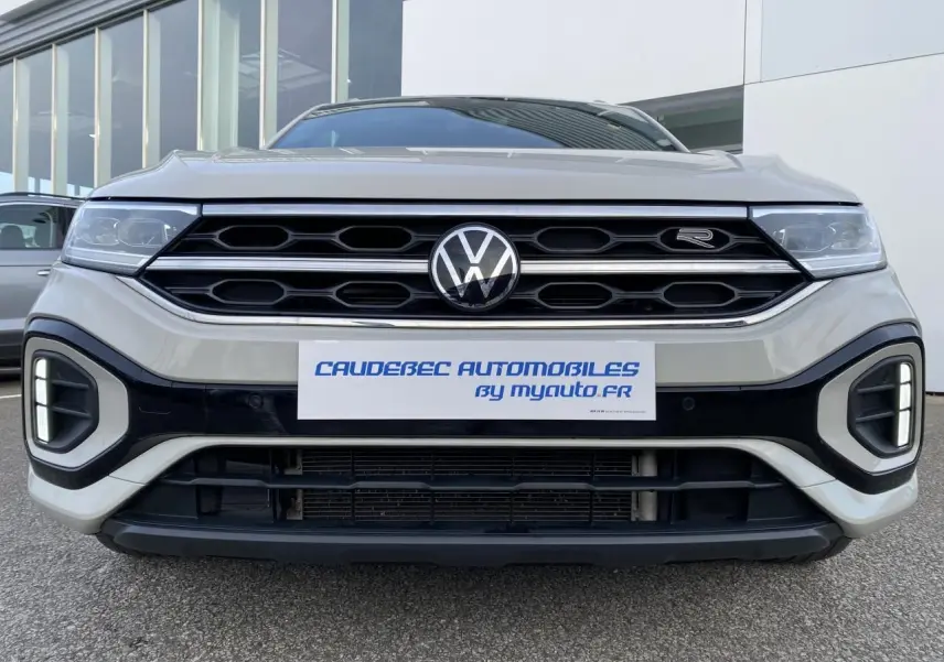 Vue frontale rapprochée du Volkswagen T-Roc gris avec calandre noire et logo R-Line visible sur la grille.